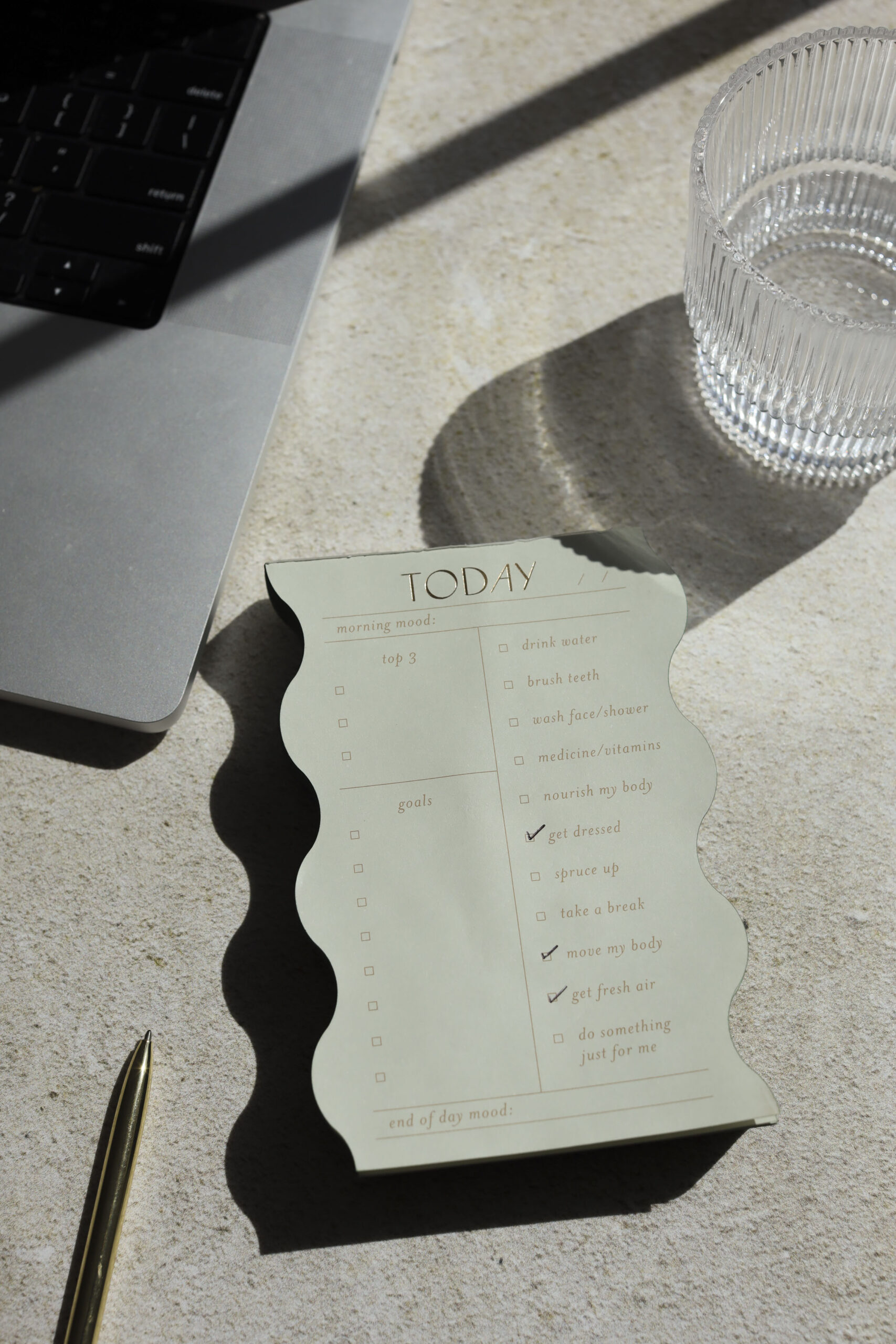 Close-up of a to-do list pad, laptop, and glass of water, symbolizing the organization and planning needed for a website launch.