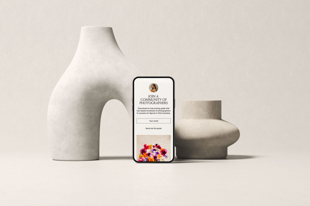 Phone mockup featuring a Flodesk form titled ‘Join a Community of Photographers,’ offering a free pricing guide download with first name and email fields, styled with two sculptural ceramic vases.